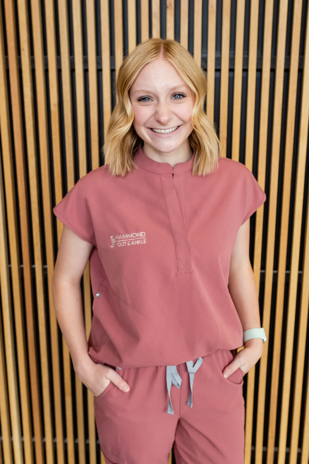 A woman in pink scrubs standing next to a wall.