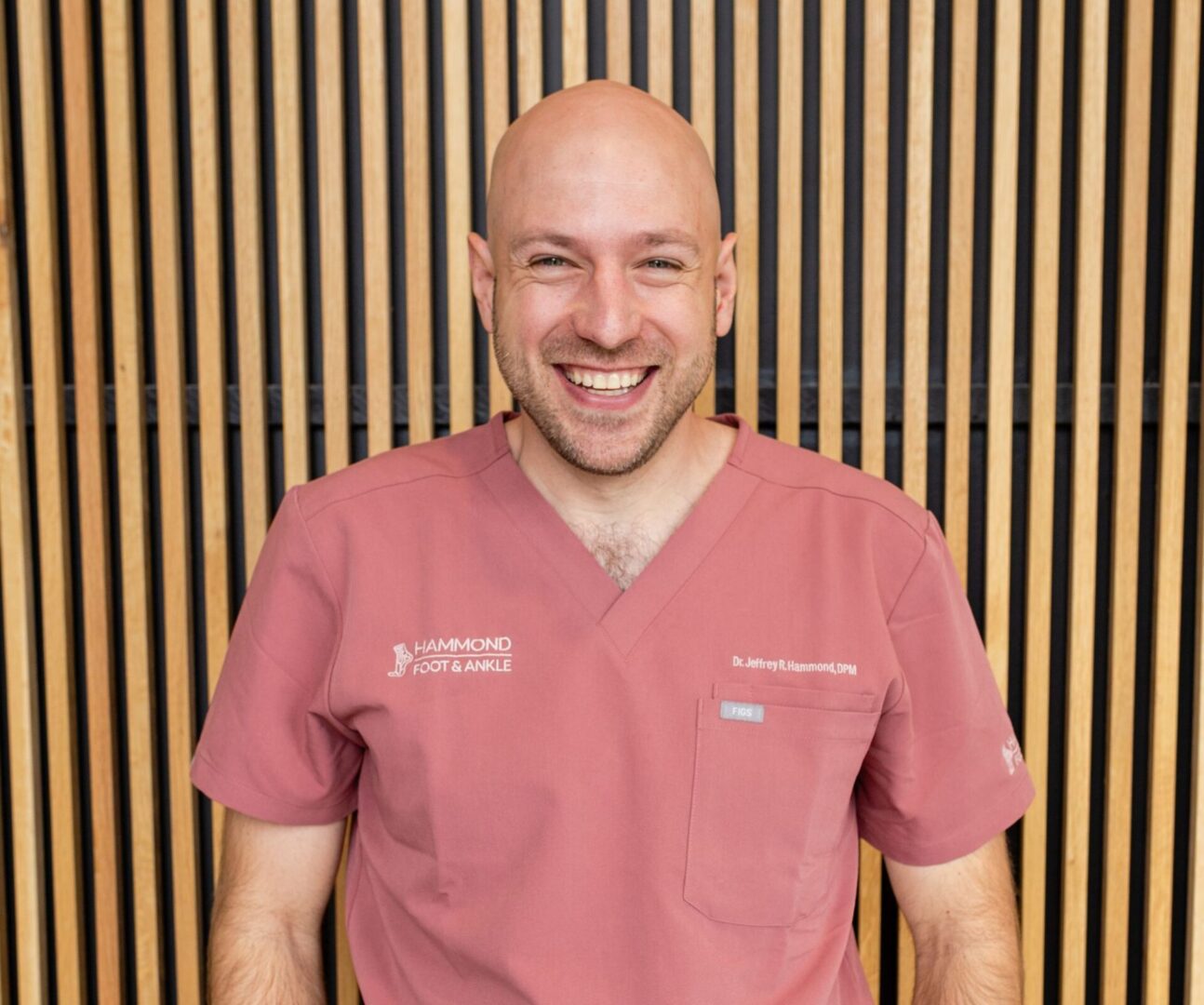 A man in pink scrubs smiling for the camera.